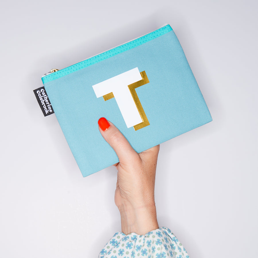 HAND HOLDING MEDIUM COTTON TURQUOISE PURSE WITH A WHITE LETTER T ON IT