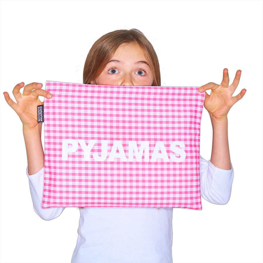 Catherine Colebrook pink gingham pyjama case with bold white ‘pyjamas' text on the front being held by young girl